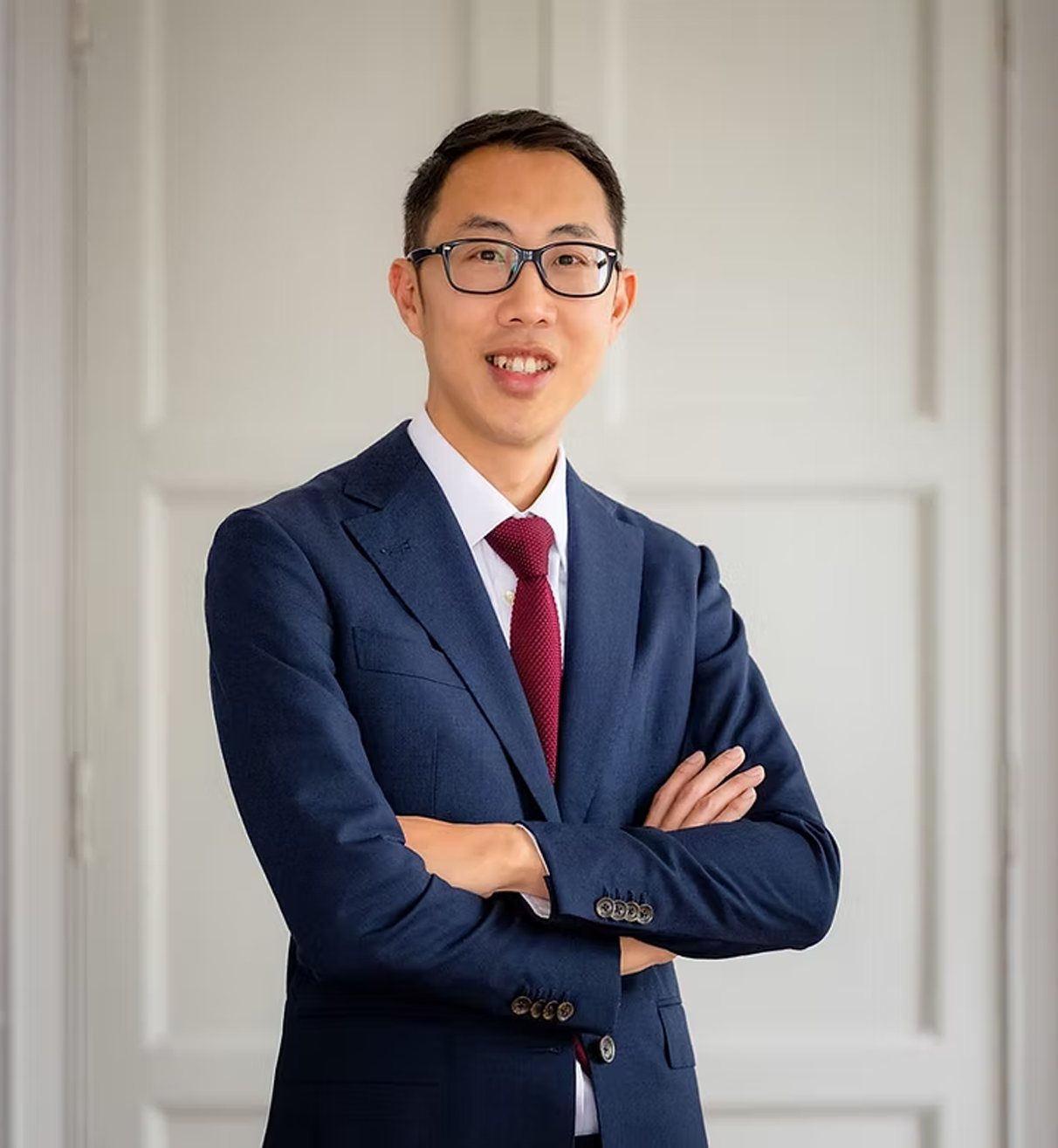 Portrait in a navy suit and red tie, arms crossed