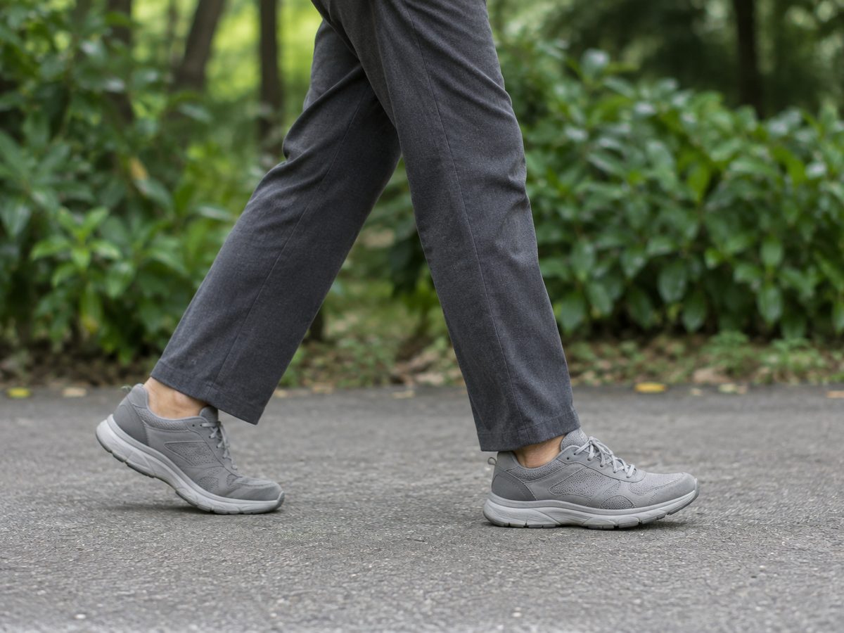 Legs in grey trousers and sports shoes, walking along a park footpath